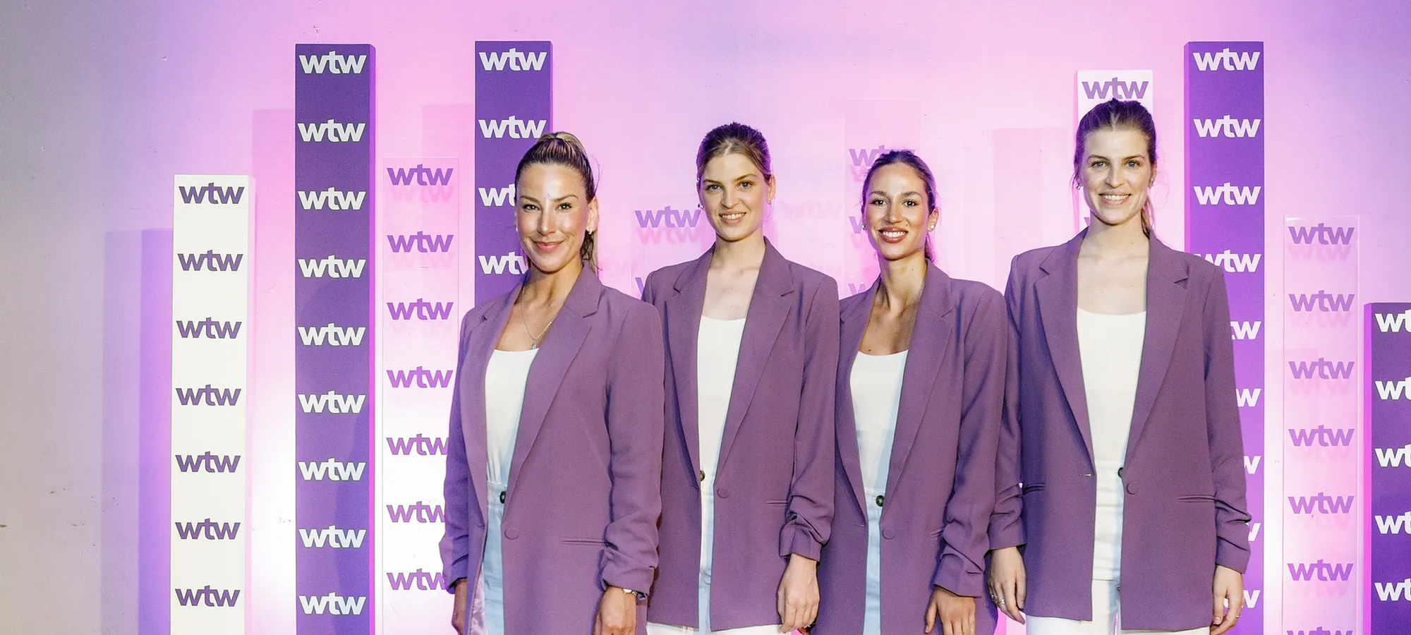Cuatro anfitrionas de pie frente al photocall de un evento corporativo